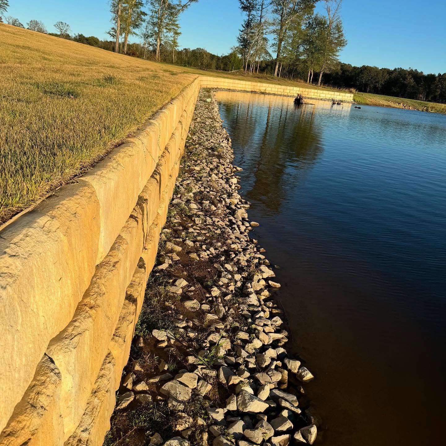 Finished pond retaining wall with a grass bank and stone along the water